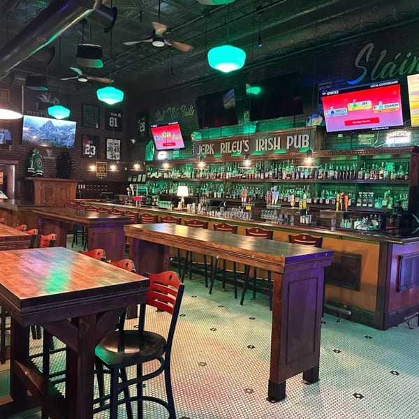 Interior of Jerk Riley's Irish Pub with a long bar, high-top tables, and green lighting.