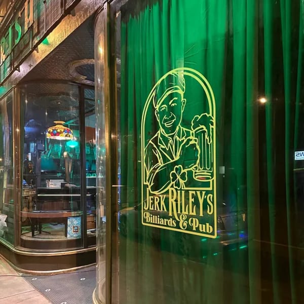 Exterior of Jerk Riley's Billiards & Pub with a green curtain and neon logo on the window.