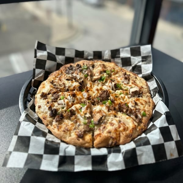 A round pizza with meat, mushrooms, and green onions on checkered paper in a black basket.