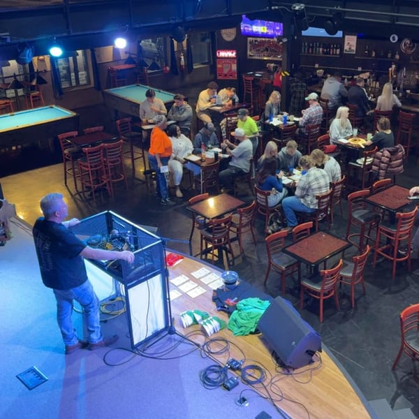 Overhead view of a lively bar with people dining, playing pool, and a DJ on stage.