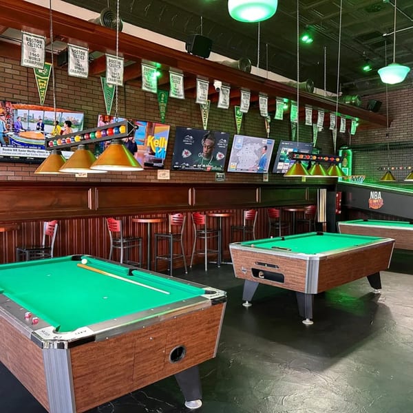 A sports bar with pool tables, high-top seating, multiple TVs, and Boston Celtics championship banners.