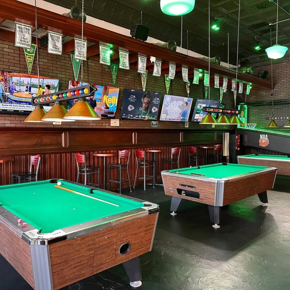 A sports bar with pool tables, high-top seating, multiple TVs, and Boston Celtics championship banners.