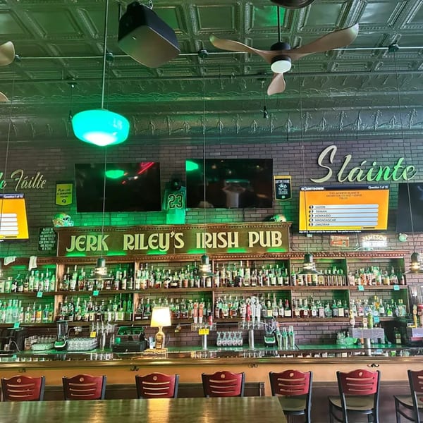 Interior of Jerk Riley's Irish Pub, featuring a fully stocked bar, green lighting, and bar stools.