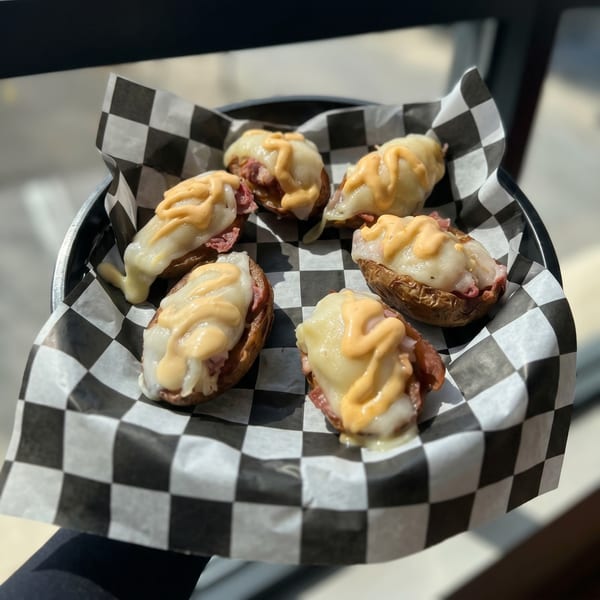 Six loaded potato skins with melted cheese and sauce on checkered paper in a black basket.