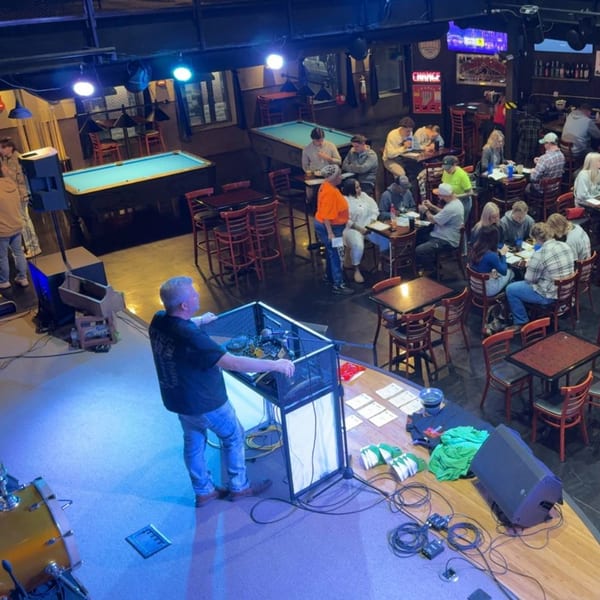 Overhead view of a lively bar with people at tables, two pool tables, and a DJ on stage.