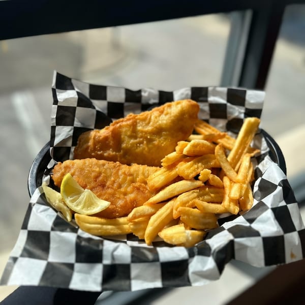 Golden-brown fish and chips with lemon wedges in a black and white checkered paper-lined basket.