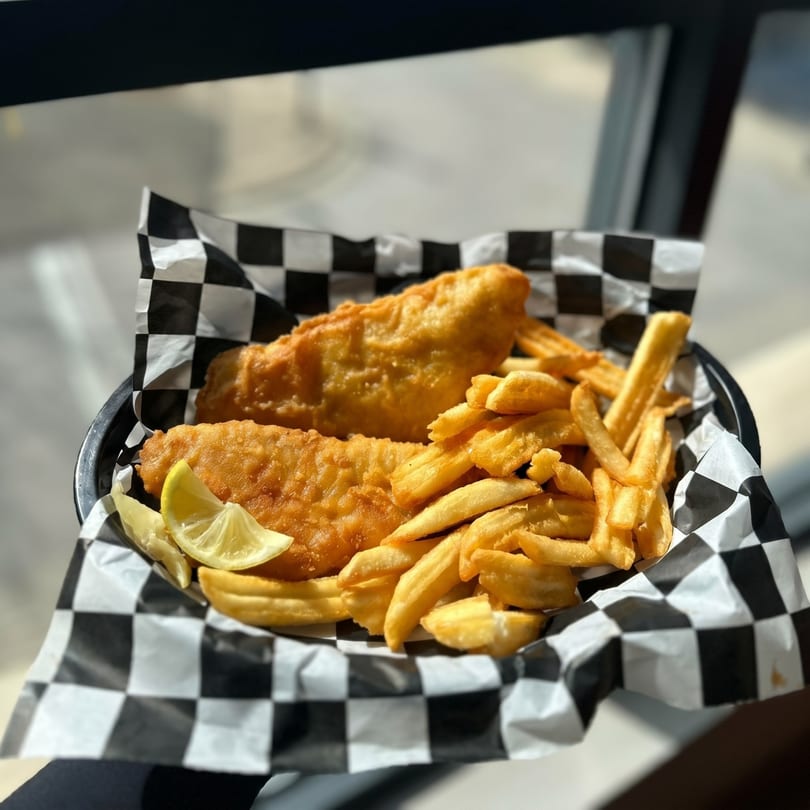 Golden-brown fish and chips with lemon wedges in a black and white checkered paper-lined basket.