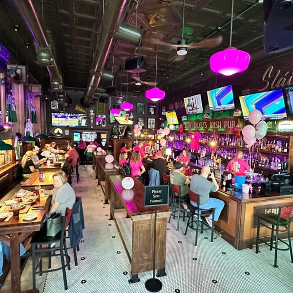 A lively Irish pub interior with patrons dining, drinking at the bar, and watching sports on multiple TVs.